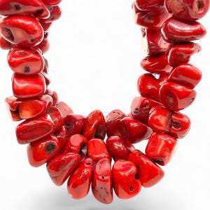 May include: A vibrant red coral necklace. The necklace is composed of irregularly shaped, polished coral beads. The beads are strung together, creating a bold and eye-catching piece of jewelry. The coral has a natural, organic appearance.