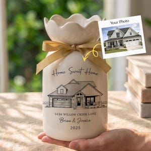 May include: A white ceramic vase with a scalloped top and a gold ribbon. The vase features a house illustration, the text "Home Sweet Home", address, names, and a year. A photo of a house is attached.