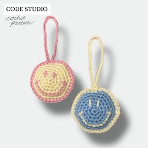 Peut inclure: Deux ornements de visage souriant crochetés. L'un est jaune avec une bordure et une boucle roses, l'autre est bleu avec une bordure et une boucle jaunes. Le texte "CODE STUDIO Crochet Pattern" est dans le coin supérieur gauche.