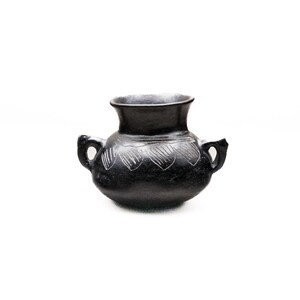Può includere: Un vaso in ceramica nera con due manici e un'ampia apertura. Il vaso presenta un motivo decorativo di linee incise attorno al corpo. Il vaso è di colore antracite scuro e si trova su uno sfondo bianco.