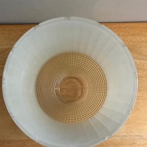 May include: A round glass light fixture shade featuring a frosted white outer rim with vertical fluted detailing and a clear amber-colored center section with a concentric grid pattern. The bowl-shaped glass shade has a smooth, circular opening.