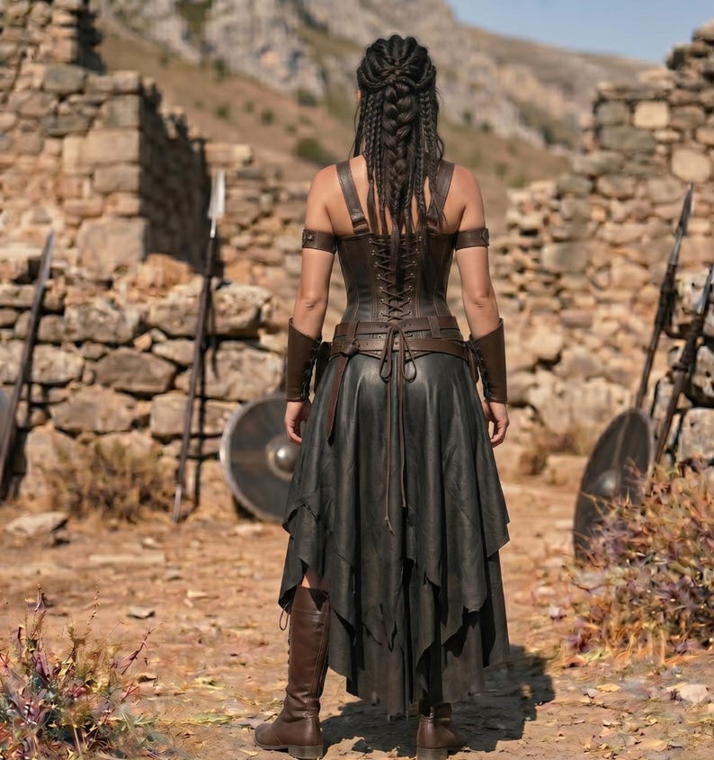May include: A dark brown leather corset with back lacing, paired with a layered black skirt. The outfit includes matching brown leather arm guards and upper arm bands. The ensemble is completed with tall brown leather boots, showcasing a structured design with multiple straps and ties visible from the back view.