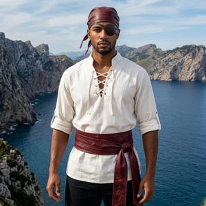 May include: A cream-colored long-sleeve shirt with a lace-up front, paired with a wide, dark red leather-like sash tied at the waist. The outfit includes a matching dark red headscarf and a black eye patch worn over one eye.