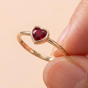 Puede incluir: Un anillo de oro de 14 quilates con una piedra preciosa roja en forma de corazón en un engaste de bisel. La banda es delgada y pulida, con el texto 14K claramente grabado en la superficie interior de la banda de oro, mostrando un diseño simple.