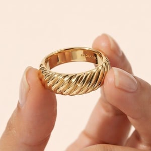 Puede incluir: Un anillo de oro con una textura pulida y retorcida similar a una cuerda alrededor de la banda exterior. El interior de la banda es liso y muestra claramente el texto grabado 14K, indicando la pureza del metal de esta joya circular.