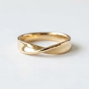 Puede incluir: Un anillo de oro pulido con un diseño trenzado continuo que crea una banda suave y fluida. El metal tiene una superficie reflectante que capta la luz, resaltando las elegantes curvas de la forma circular de esta pieza de joyería.