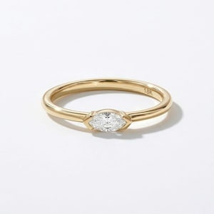 May include: A gold ring with a marquise-cut diamond center stone. The ring has a thin band and is set in a bezel setting. The ring is marked with "18K".