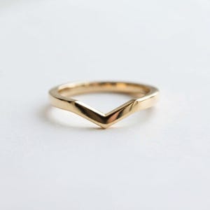 Pode incluir: Um anel de ouro polido com um design em forma de V ou chevron. A banda tem uma superfície lisa e contínua com um acabamento metálico reflexivo que se estreita até um ponto no centro, criando uma silhueta angular distinta para a peça.