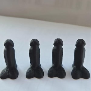 Puede incluir: Cuatro pequeñas figuras de color negro mate impresas en tres dimensiones, cada una con una forma fálica con una parte superior redondeada y una base más ancha. La superficie de cada objeto muestra líneas de capa horizontales visibles.