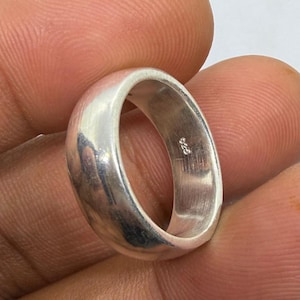 Puede incluir: Un anillo de plata pulida con un diseño liso y redondeado. El anillo es una banda sólida, que refleja la luz y muestra un brillo sutil. El interior del anillo está marcado con "925".