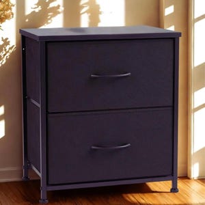 May include: A two-drawer storage unit with a dark purple fabric front and a dark metal frame. The drawers have curved handles. The unit is on short legs and is against a light-colored wall.