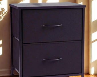 Puede incluir: Una unidad de almacenamiento de dos cajones con frente de tela morada oscura y marco de metal oscuro. Los cajones tienen tiradores curvos. La unidad está sobre patas cortas y contra una pared de color claro.