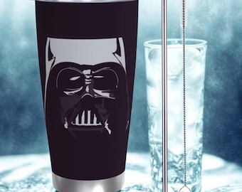 Puede incluir: Un vaso térmico negro de acero inoxidable con un gráfico blanco de la cara de Darth Vader. Una pajita de acero inoxidable y un vaso de agua están junto al vaso. El vaso tiene un borde y una tapa plateados.