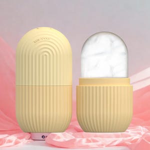 K&ouml;nnte beinhalten: Zwei gelbe, kapself&ouml;rmige Beauty-Tools. Eines ist geschlossen, das andere offen und zeigt eine wei&szlig;e, eisartige Substanz. Beide haben vertikale Rippendetails. Das geschlossene Werkzeug hat das Wort "Night" und ein wellenf&ouml;rmiges Liniendesign.