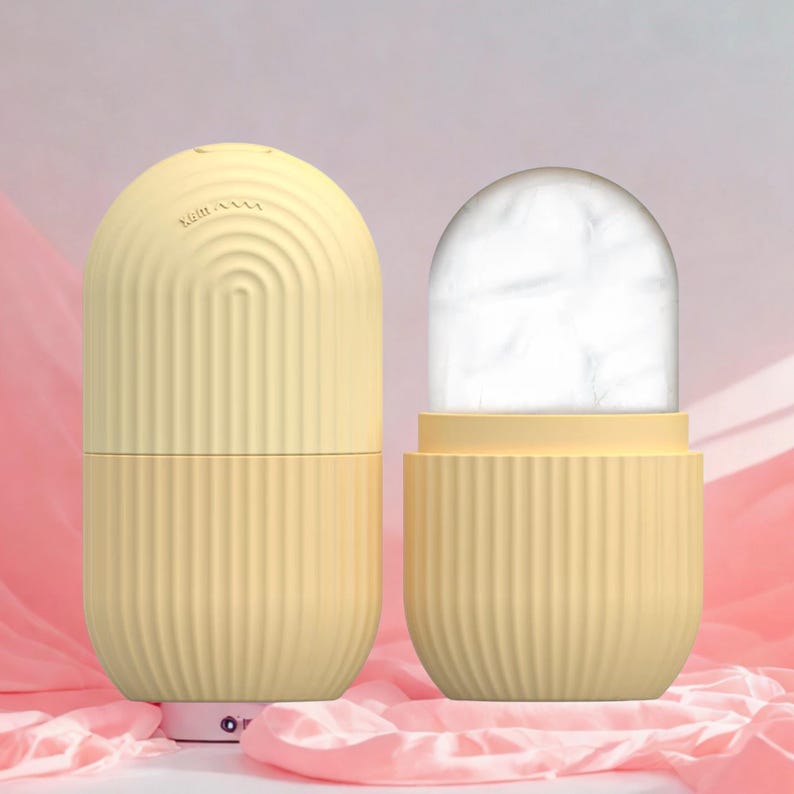 K&ouml;nnte beinhalten: Zwei gelbe, kapself&ouml;rmige Beauty-Tools. Eines ist geschlossen, das andere offen und zeigt eine wei&szlig;e, eisartige Substanz. Beide haben vertikale Rippendetails. Das geschlossene Werkzeug hat das Wort "Night" und ein wellenf&ouml;rmiges Liniendesign.