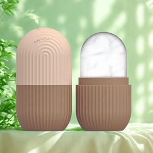 K&ouml;nnte beinhalten: Zweiteilige Gesichts-Eisroller in einer sanften Farbpalette. Die obere H&auml;lfte ist hellpfirsichfarben mit einem geschwungenen Design, und die untere H&auml;lfte ist braun mit vertikalen Linien. Die zweite Rolle ist offen und zeigt ein wei&szlig;es, eisiges Inneres.