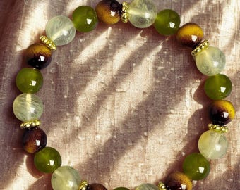 Puede incluir: Una pulsera de cuentas con esferas redondas alternas en tonos verde oliva, amarillo pálido translúcido y marrón oscuro con efecto degradado. El diseño incluye pequeñas cuentas espaciadoras de metal dorado texturizado entre las esferas.