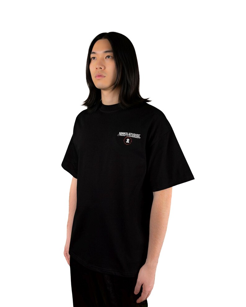 May include: Black t-shirt with the text "SONKEL STUDIOS" in white and a small circular logo. The shirt is a solid black color and has short sleeves. The model is wearing black pants.