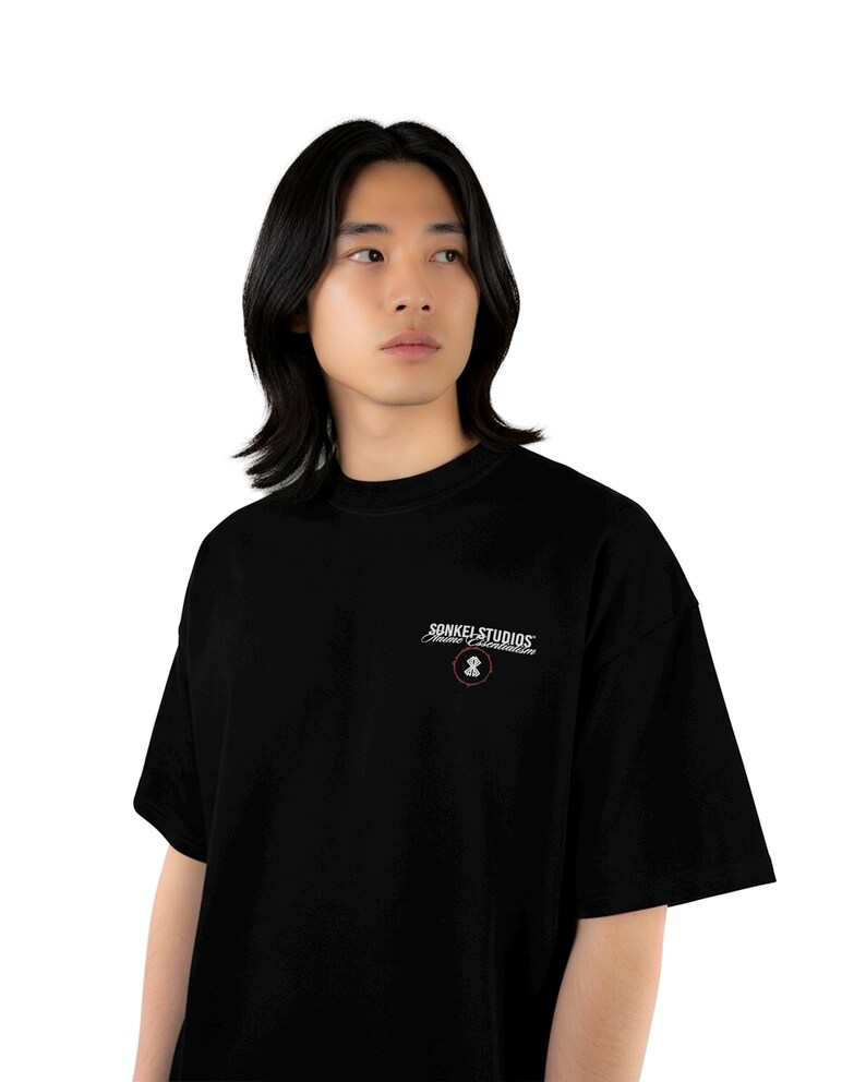 May include: Black t-shirt with the text "SONKEL STUDIOS" in white script above a small graphic. The shirt has a crew neck and short sleeves. The model is wearing the shirt.
