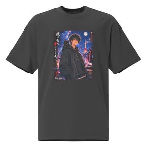 Könnte beinhalten: Ein anthrazitfarbenes Kurzarm-T-Shirt mit einem rechteckigen Grafikdruck eines Anime-Charakters mit einer schwarzen Katze auf der Schulter vor einer nächtlichen Stadtkulisse. Der Text lautet "夜は長い。夢はもっと長い" und "REN KADO".