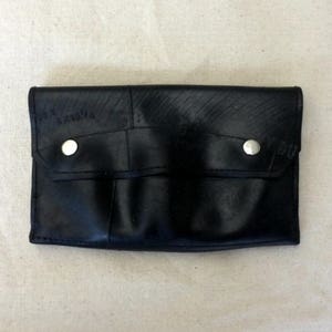 May include: A black leather wallet made from recycled tire inner tubes. The wallet has two snap closures and a flap with a pocket.