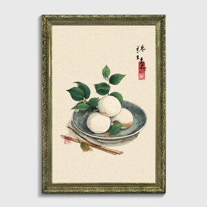 Puede incluir: Una impresión enmarcada que presenta una naturaleza muerta de bolas de mochi blancas sobre un plato azul, adornada con hojas verdes. Palillos y una ramita de hojas se colocan junto al plato. Caracteres japoneses y un sello rojo en la esquina superior derecha.