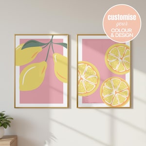 May include: Two framed wall art prints with gold frames. The left print features yellow lemons on a branch with green leaves against a pink background. The right print shows three sliced lemon halves on a pink background. Text reads: customise your COLOUR & DESIGN.