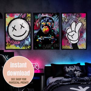 Puede incluir: Un conjunto de tres láminas rectangulares para pared con un fondo de estilo grafiti. La lámina izquierda muestra una cara sonriente blanca con ojos en forma de X. La central representa un chimpancé con auriculares sosteniendo un mando. La derecha muestra una mano de dibujos animados blanca haciendo el signo de la paz.