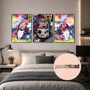 May include: A triptych wall art set featuring vibrant graffiti-style artwork. The left and right panels display white game controllers, while the centre panel shows a handheld gaming console with the name THEO written in colourful letters.