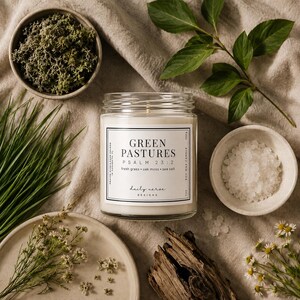 May include: A soy wax candle in a glass jar with a label that reads "Green Pastures Psalm 23:2". The candle is surrounded by decorative elements including moss, grass, sea salt, and flowers. The candle is 200g.