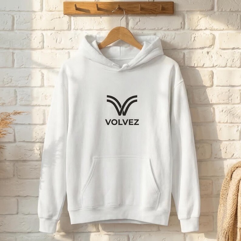 May include: White hoodie with a front pocket and a drawstring hood. The hoodie features a black graphic of two curved lines forming a V shape, with the word "VOLVEZ" below it. The hoodie is hanging on a wooden hanger.