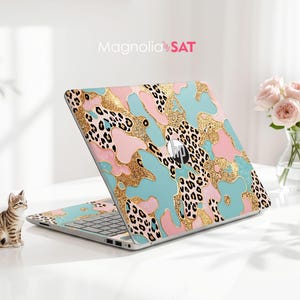 May include: An HP laptop featuring a decorative skin with a pattern of light blue, pink, and gold glitter shapes interspersed with black and white leopard print spots. The brand logo is centered on the lid, and the text Magnolia SAT is visible.
