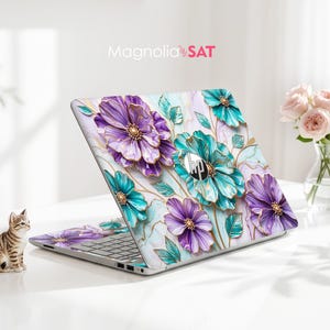 May include: An HP laptop featuring a decorative skin with a vibrant floral pattern of purple and teal flowers against a white marble background. The design includes gold-toned outlines on the petals and leaves. The text Magnolia SAT is visible.