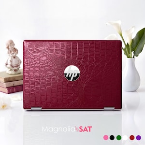 Op de afbeelding: Een donker magenta laptop met een glanzend, getextureerd krokodillenleerpatroon op de deksel. In het midden van de deksel bevindt zich een rond zilverkleurig HP-logo. De laptop is gesloten en horizontaal geplaatst met een reptielachtig schubbenpatroon.