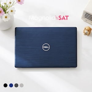 Op de afbeelding: Een gesloten donkerblauwe Dell-laptop met een geborstelde metalen textuur op het deksel en een gecentreerd wit Dell-logo. De laptop staat op een witte ondergrond naast een vaas met witte bloemen, een klein hondenbeeldje en de tekst Magnolia SAT.