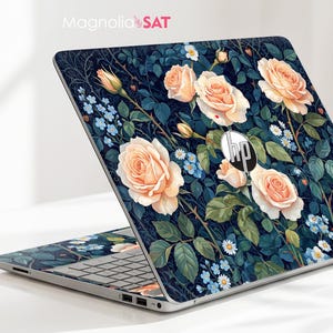Puede incluir: Un ordenador portátil HP con una cubierta decorativa de fondo azul marino oscuro, decorada con rosas color melocotón, pequeñas flores nomeolvides azules y margaritas blancas. El texto Magnolia SAT es visible en la esquina superior izquierda.
