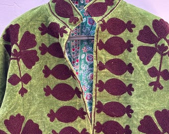 May include: A light green jacket featuring dark maroon floral and pomegranate-shaped embroidery. The garment has a high collar and an open front, revealing a contrasting inner lining with a multi-colored floral and geometric pattern.