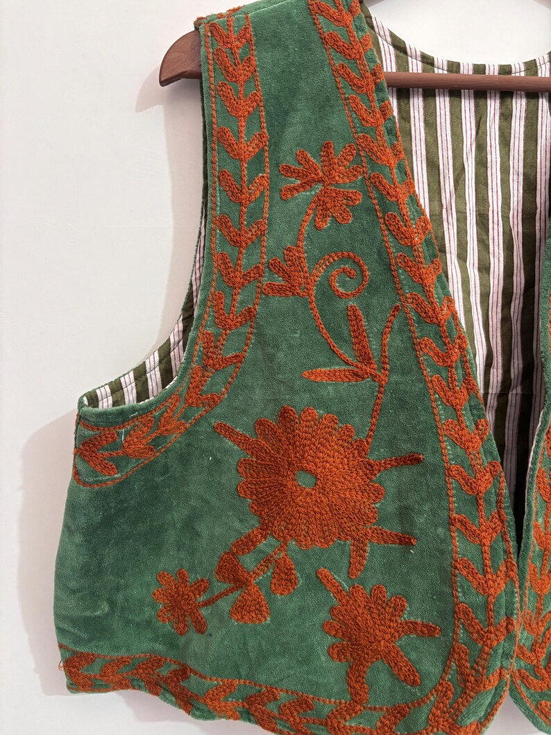 Puede incluir: Un chaleco verde con bordado floral color &oacute;xido. El chaleco tiene un forro a rayas en tonos verdes y blancos. El bordado presenta patrones detallados de flores y hojas, agregando un toque decorativo a la prenda.