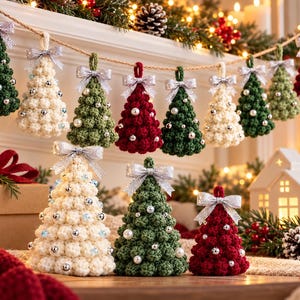 May include: A collection of crocheted Christmas tree ornaments in red, green, and cream, featuring silver bows and small pearl-like beads. Some trees hang from a twine string, while others stand upright on a surface with festive decor.