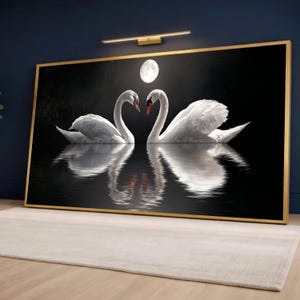 Può includere: Stampa su tela incorniciata con due cigni bianchi con becchi rossi, che formano un cuore, riflessi nell'acqua. Una luna piena è visibile sopra i cigni su sfondo nero. La cornice è dorata.
