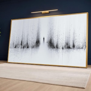 May include: A framed art print with a gold frame. The artwork is a black and white abstract image of a person walking on a path. The path is surrounded by vertical lines and dots. A gold-coloured light fixture is mounted above the artwork.
