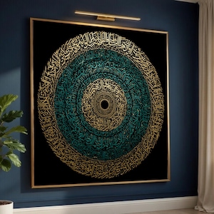 May include: A framed artwork featuring a circular design of Arabic calligraphy in gold and teal against a black background. The artwork is mounted in a gold frame and hangs on a dark blue wall.