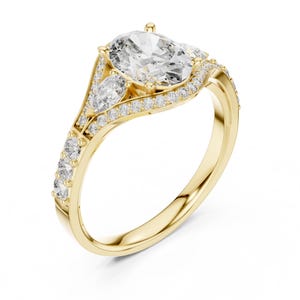 May include: A yellow gold ring featuring a large oval-cut centre stone, flanked by two pear-shaped side stones. The band and setting are accented with small round pavé-set diamonds that follow the curve of the gold metal structure.
