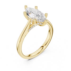 May include: A yellow gold ring featuring a large marquise-cut clear centre stone held by six prongs. The band includes a row of small pavé-set clear stones along the upper shoulders, leading up to the central setting in a polished finish.