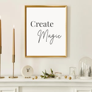 Peut inclure: Un cadre doré avec l'inscription "Create Magic" en noir est suspendu au-dessus d'une cheminée blanche. Deux bougeoirs dorés allumés encadrent l'impression. Une petite horloge, de la verdure et des objets décoratifs complètent l'ensemble.