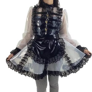 K&ouml;nnte beinhalten: Ein schwarz-wei&szlig;es Kleid mit hohem Kragen, langen &Auml;rmeln und einem mehrschichtigen Rock. Das Kleid hat ein schwarzes Oberteil mit Schlossdetails und einen schwarzen Rock im Sch&uuml;rzenstil. Der Rock hat eine wei&szlig;e Unterlage mit schwarzem Spitzensaum.