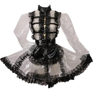 K&ouml;nnte beinhalten: Ein transparentes Kleid mit schwarzer Spitzenborte und einer schwarzen Satinschleife. Das Kleid hat einen hohen Kragen, ein schwarzes lederartiges Oberteil mit goldfarbenen Vorh&auml;ngeschl&ouml;ssern und lange, transparente &Auml;rmel. Der Rock ist mit schwarzer Spitze versehen.
