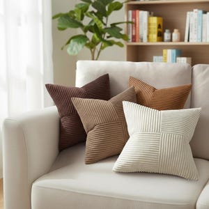 Peut inclure: Cinq coussins en velours côtelé dans des tons de marron et de crème, disposés sur un canapé crème. Les coussins présentent un motif géométrique. Un élément décoratif pour la décoration intérieure.