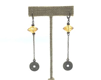 May include: A pair of dangle earrings with amber glass beads and silver coin charms. The earrings are displayed on a burlap stand.