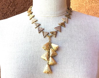 May include: A gold and brown statement necklace with a triangular pendant. The necklace is made of stone and metal.